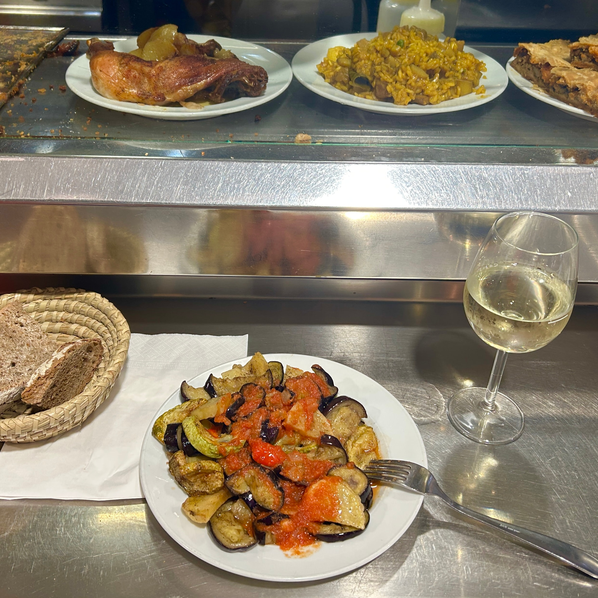 Roasted potatoes, aubergine and courgette in tomato sauce with a glass of white wine at Mercat de Santa Catalina